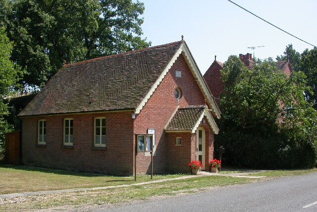 A small brick building with a pitched roof, a front porch, and red flowers in the front yard.