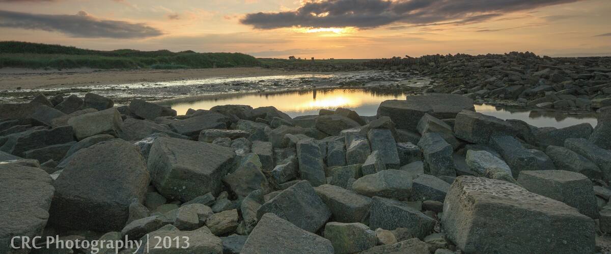 A rocky shoreline with a calm body of water reflecting the sunset sky.