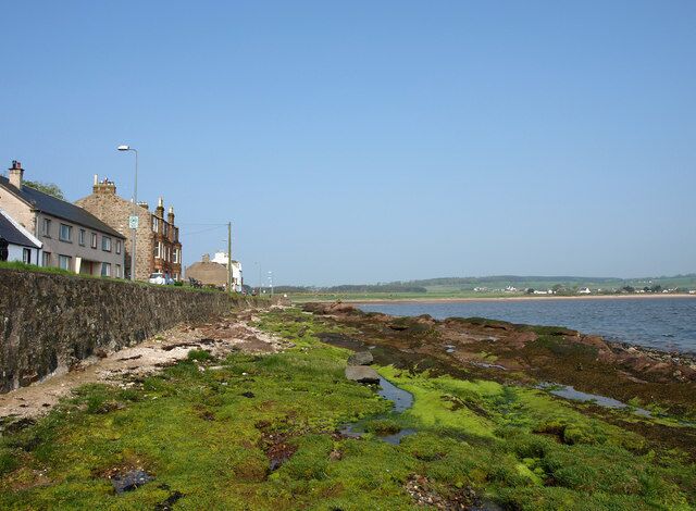 A coastal area with buildings, a rocky shoreline, and a clear sky.