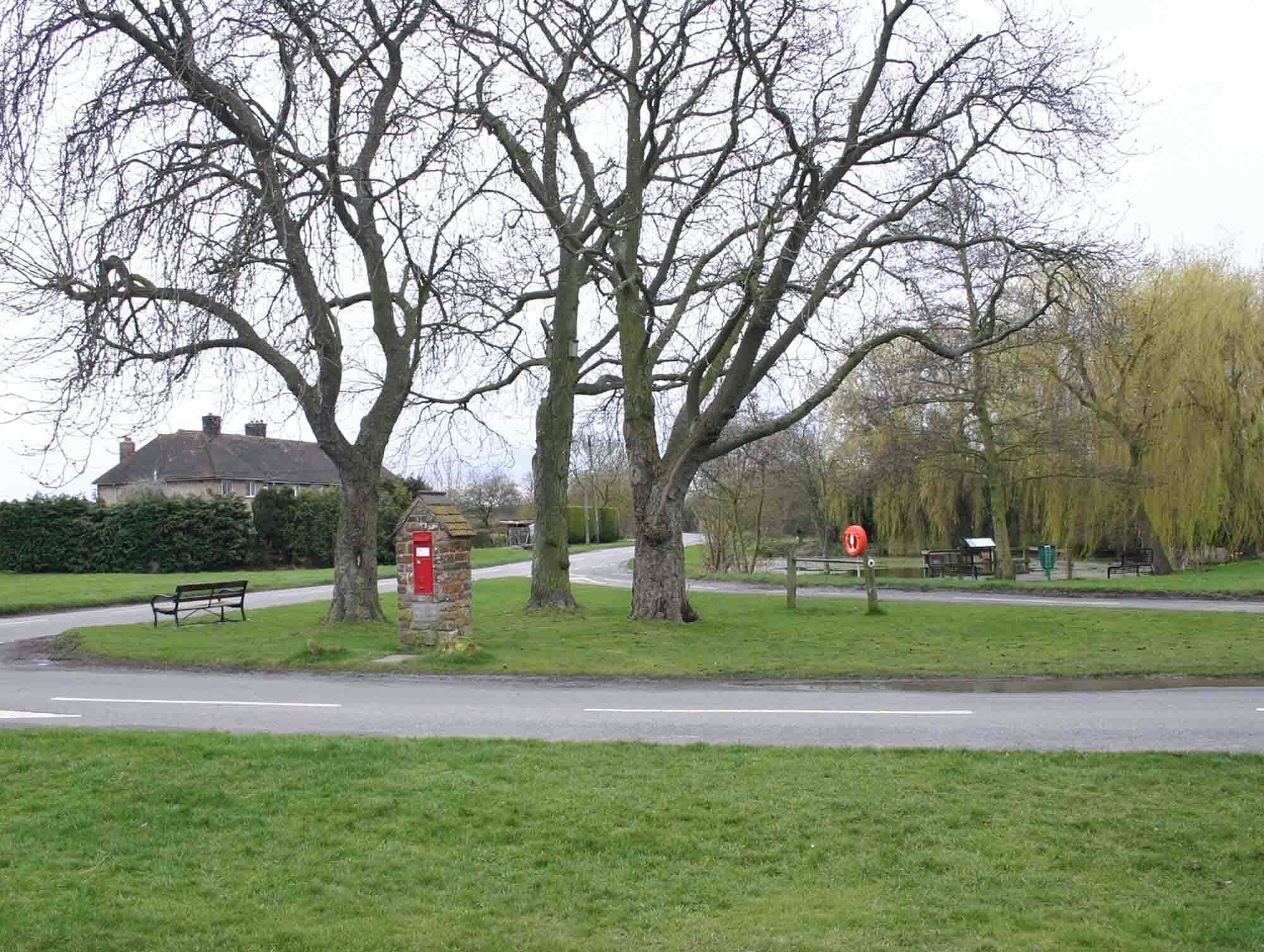 A park with a red post box, a bench, and a road with a roundabout.