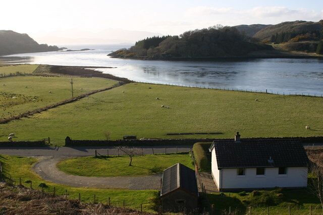 A river, green fields, a white house, and distant hills.