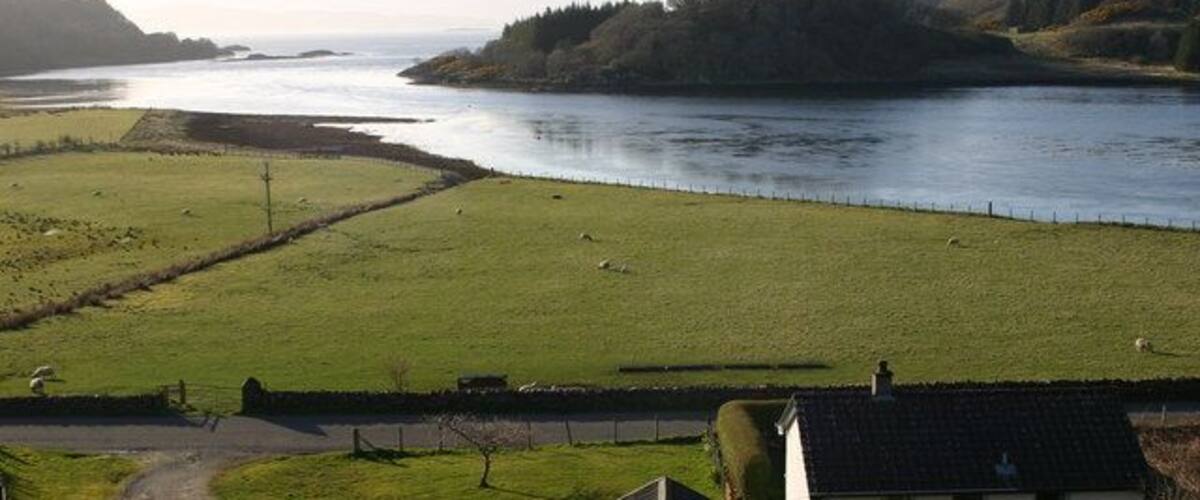A river, green fields, a white house, and distant hills.