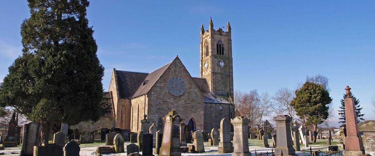 A church with a clock tower and a cemetery with gravestones.