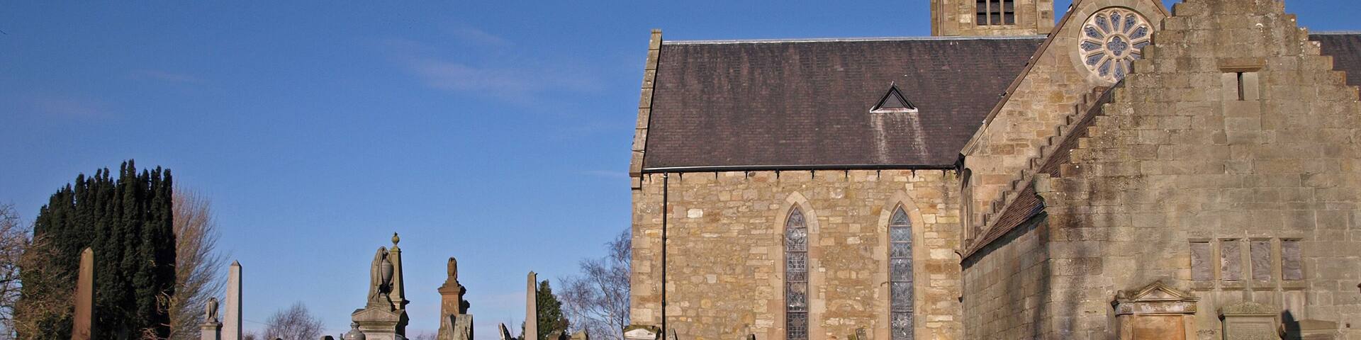 A historic church with a large rose window and a tall tower. In front of the church, there are numerous gravestones and headstones.