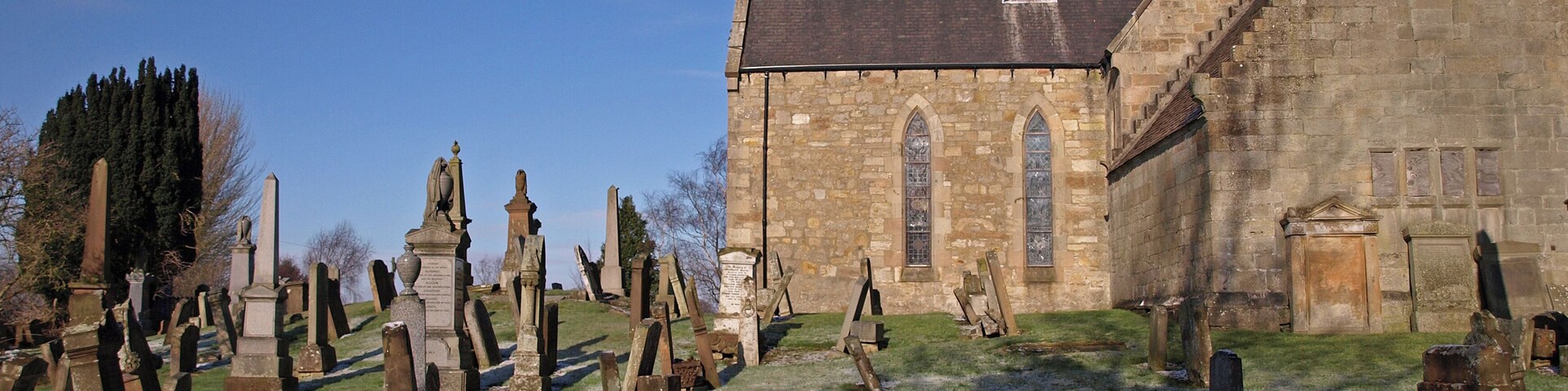 Una iglesia histórica con un gran rosetón y una torre alta. Frente a la iglesia, se encuentran numerosas lápidas y epitafios.