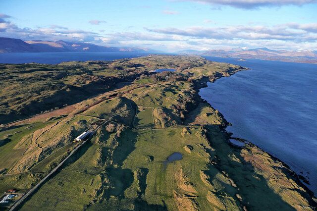 An aerial view of a coastal landscape with rolling hills, a road, and a body of water.