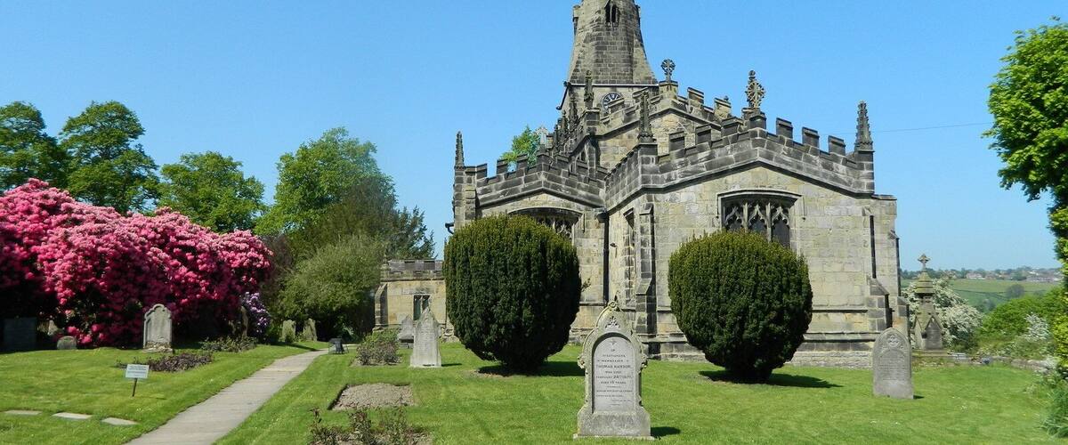A historic church with a tall spire, surrounded by well-maintained grass and flowering bushes.