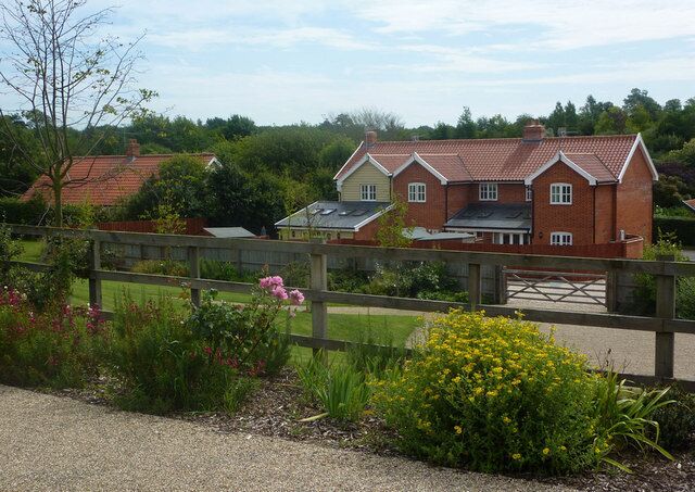 A red brick house with a white fence, surrounded by greenery and flowers.