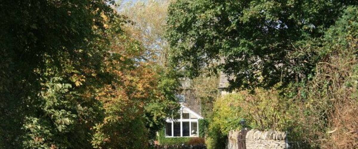 A rural pathway leading to a stone wall and a house surrounded by trees.