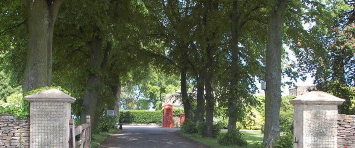 A paved driveway leading to a red gate, surrounded by trees and stone walls.
