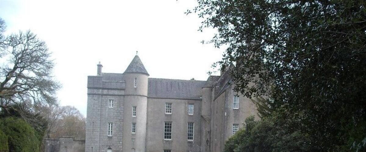 A large, historic stone building with a turret and a paved driveway leading to it.