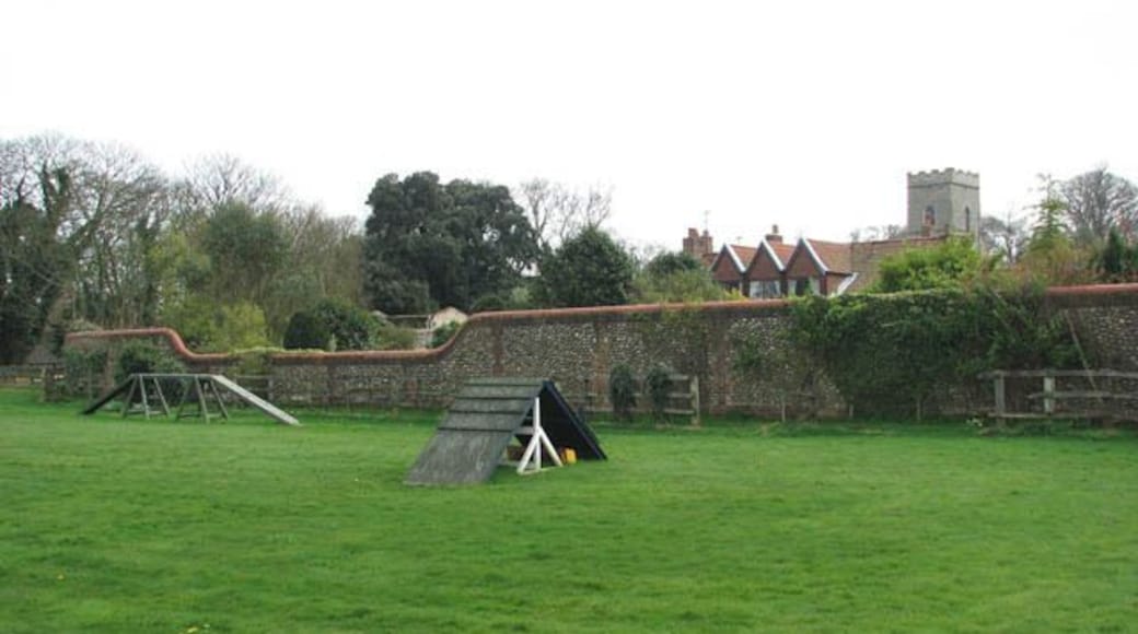 Flint and brick wall surrounding Kelling Hall. The high flint and brick wall surrounds Kelling Hall and adjoining properties. The tower of St Mary's church > 1251992 can be seen in the background. A dog training area can be seen in the foreground.