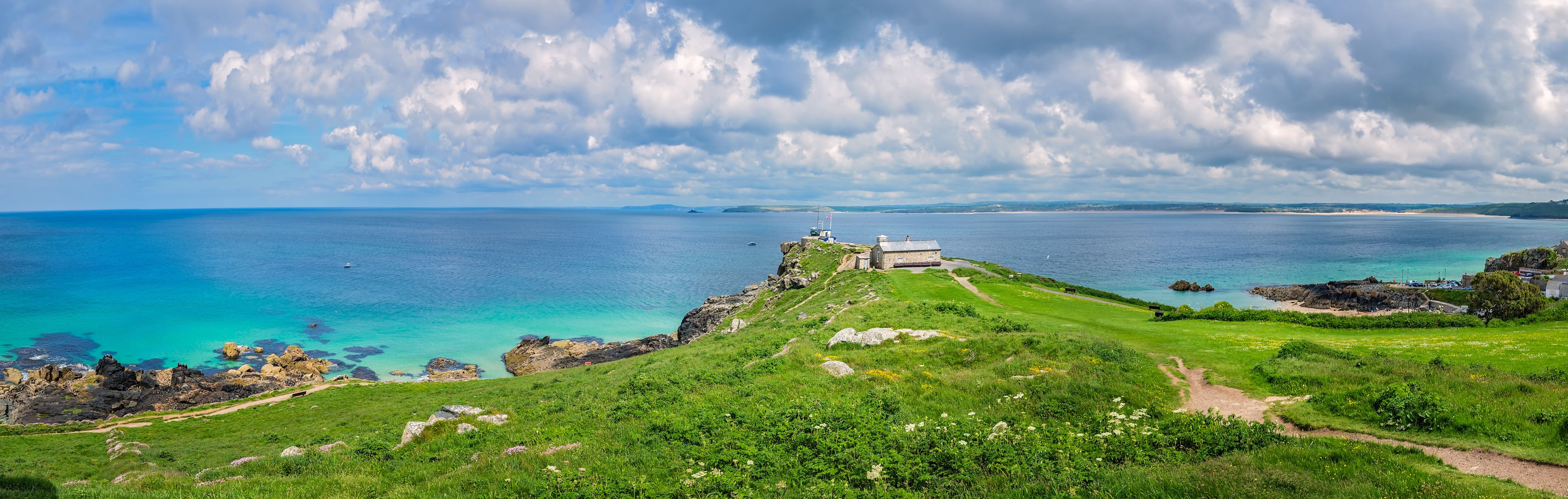 A coastal landscape with a grassy hill, a lighthouse, and the sea.