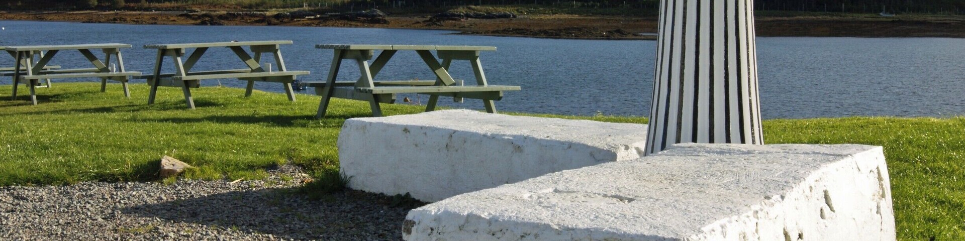 Un área de picnic junto al lago con bancos y un pilar de piedra.