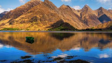 A mountain range with a lake reflecting the peaks and a small boat in the foreground.