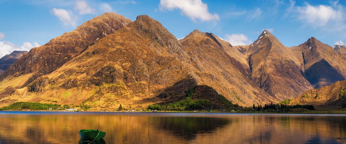 A mountain range with a lake reflecting the peaks and a small boat in the foreground.