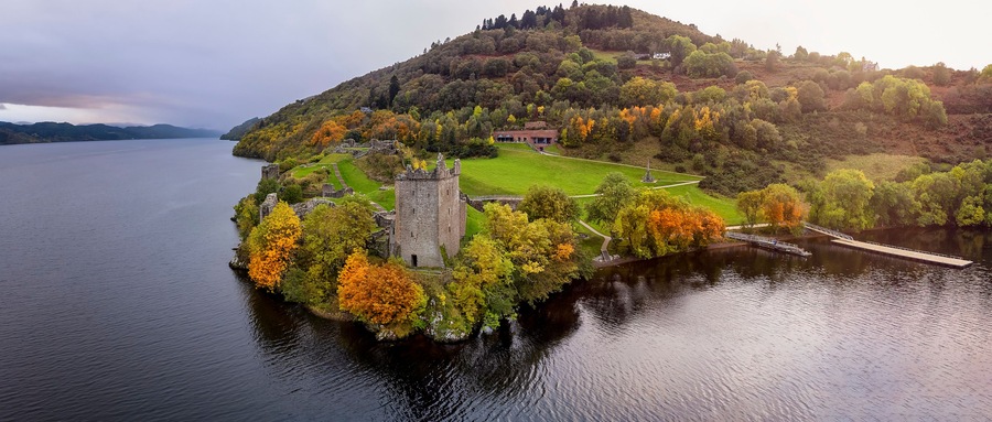 Un castillo histórico en una pequeña isla rodeada por un lago, con follaje otoñal y cielo despejado.