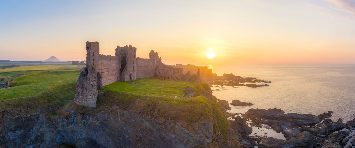 A coastal castle at sunset with a clear sky and calm sea.