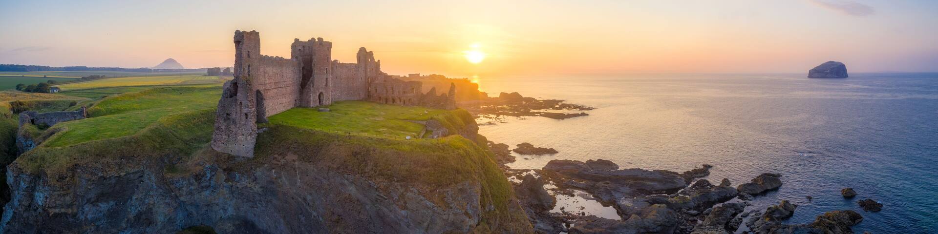 A coastal castle at sunset with a clear sky and calm sea.