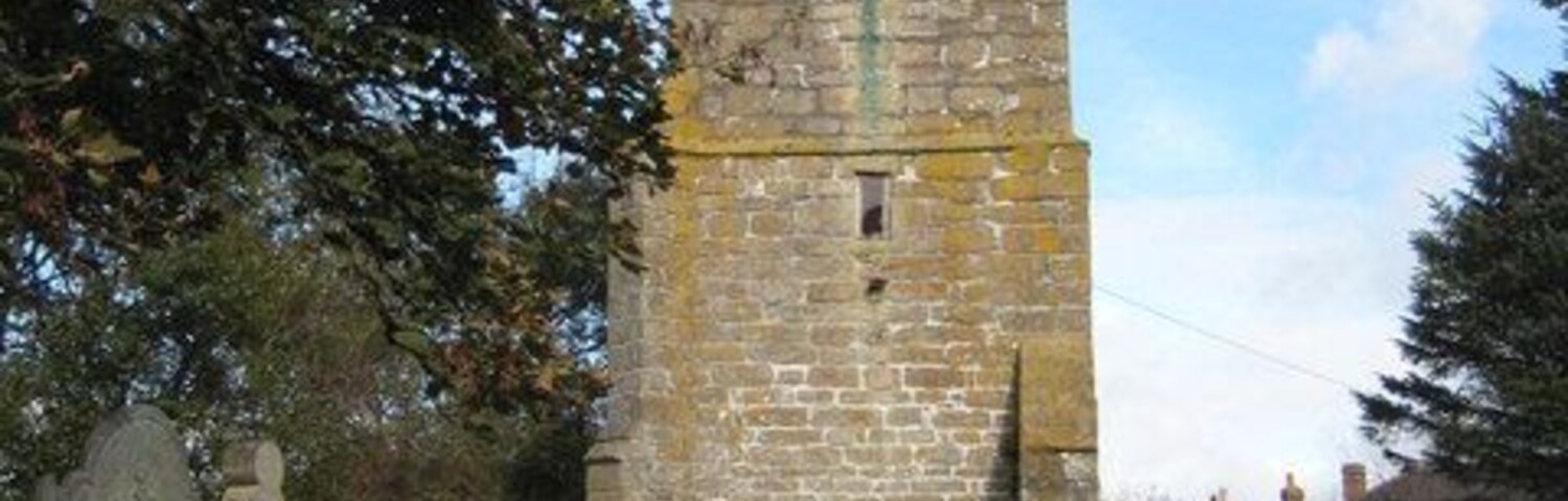 Una torre de piedra con un reloj, rodeada de lápidas en una zona cubierta de hierba.