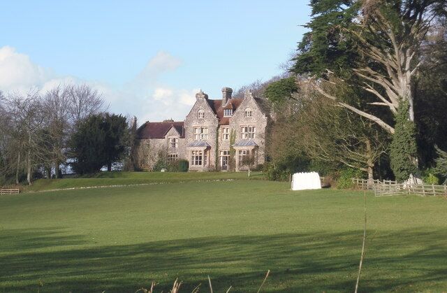 A large, historic stone building with a red roof, surrounded by a well-manicured lawn and trees.