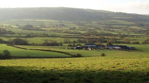 White House The farm is on the broad valley floor of the Camlad, which follows the line of trees winding across the photo just beyond, and marks the border with England. The farm is in Wales, as is the lane from which the photo was taken, descending from Bagbury towards the A489. Beyond is Aston Hill.