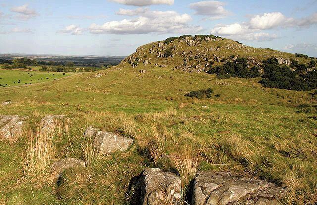 A grassy hill with scattered rocks and a distant view of a valley.