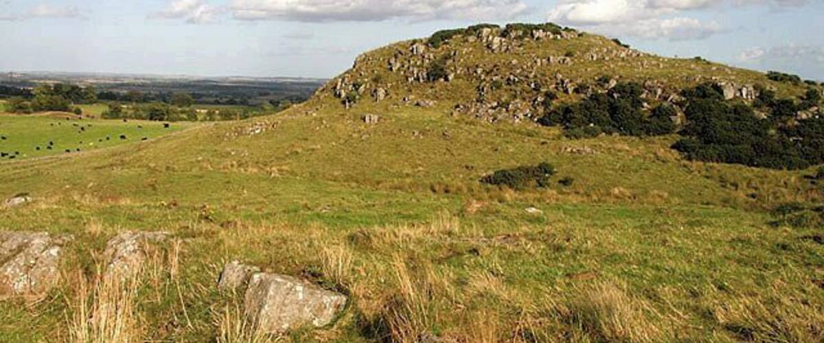 A grassy hill with scattered rocks and a distant view of a valley.