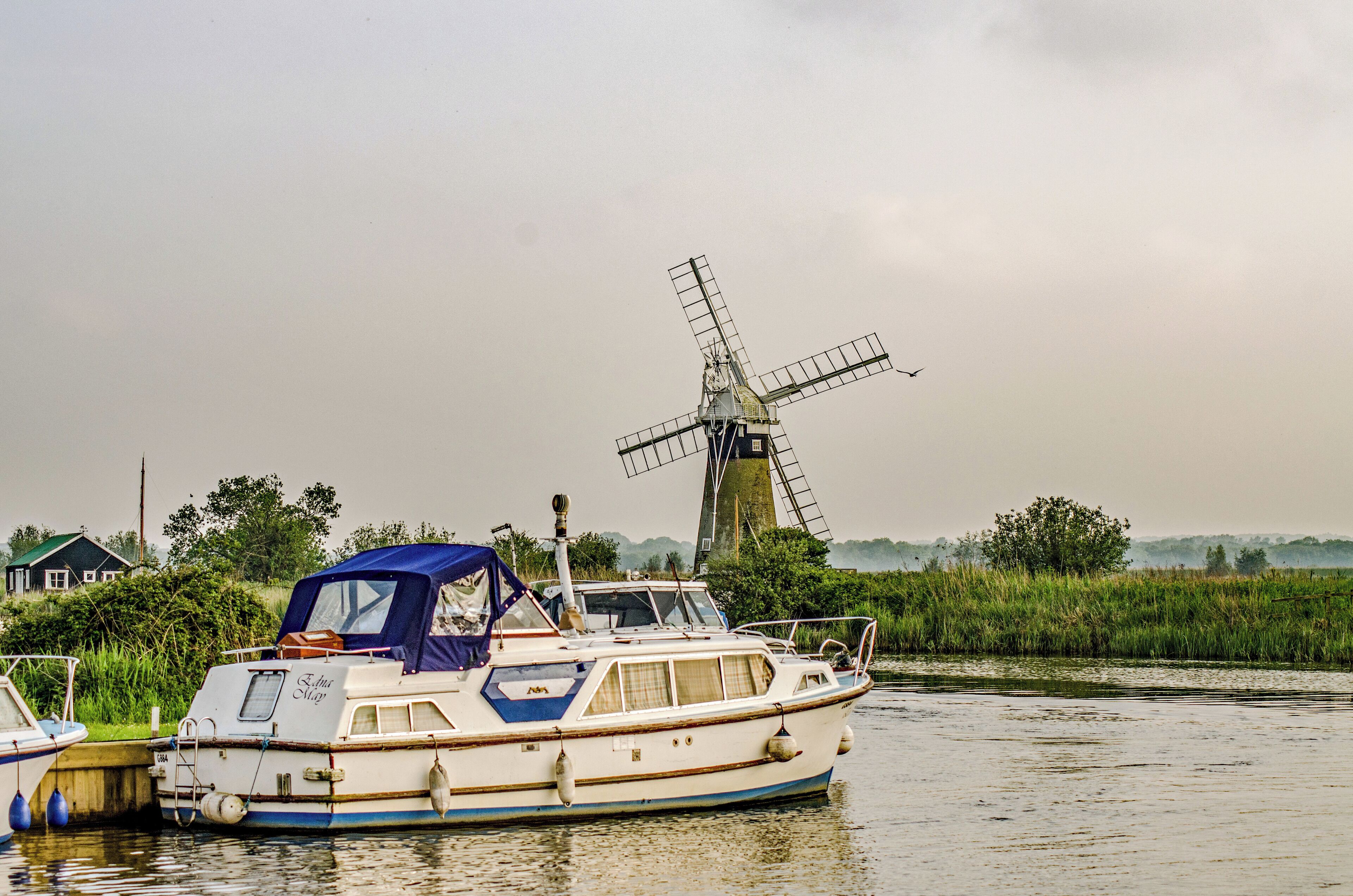 A boat docked near a windmill and a house by a river.