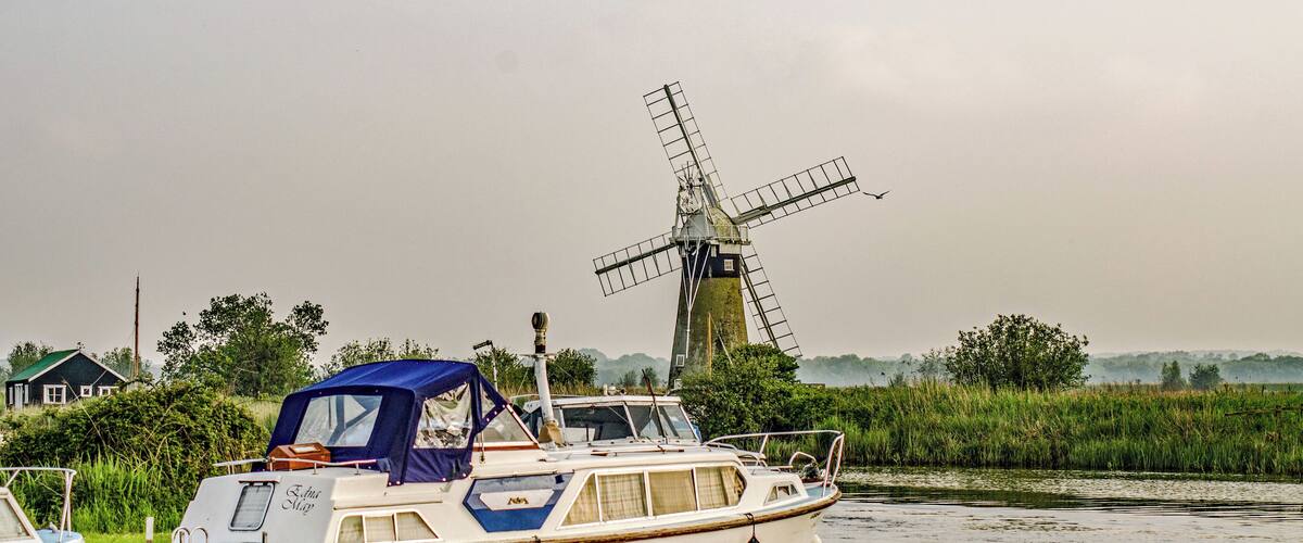 A boat docked near a windmill and a house by a river.