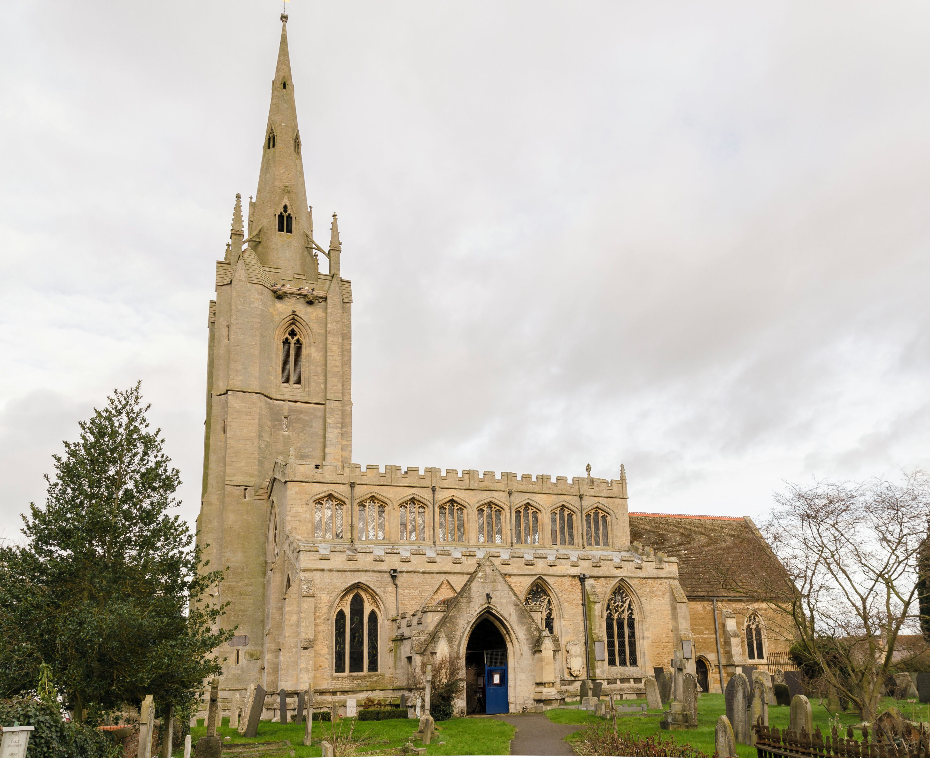 A historic church with a tall spire, arched windows, and a cemetery in front.