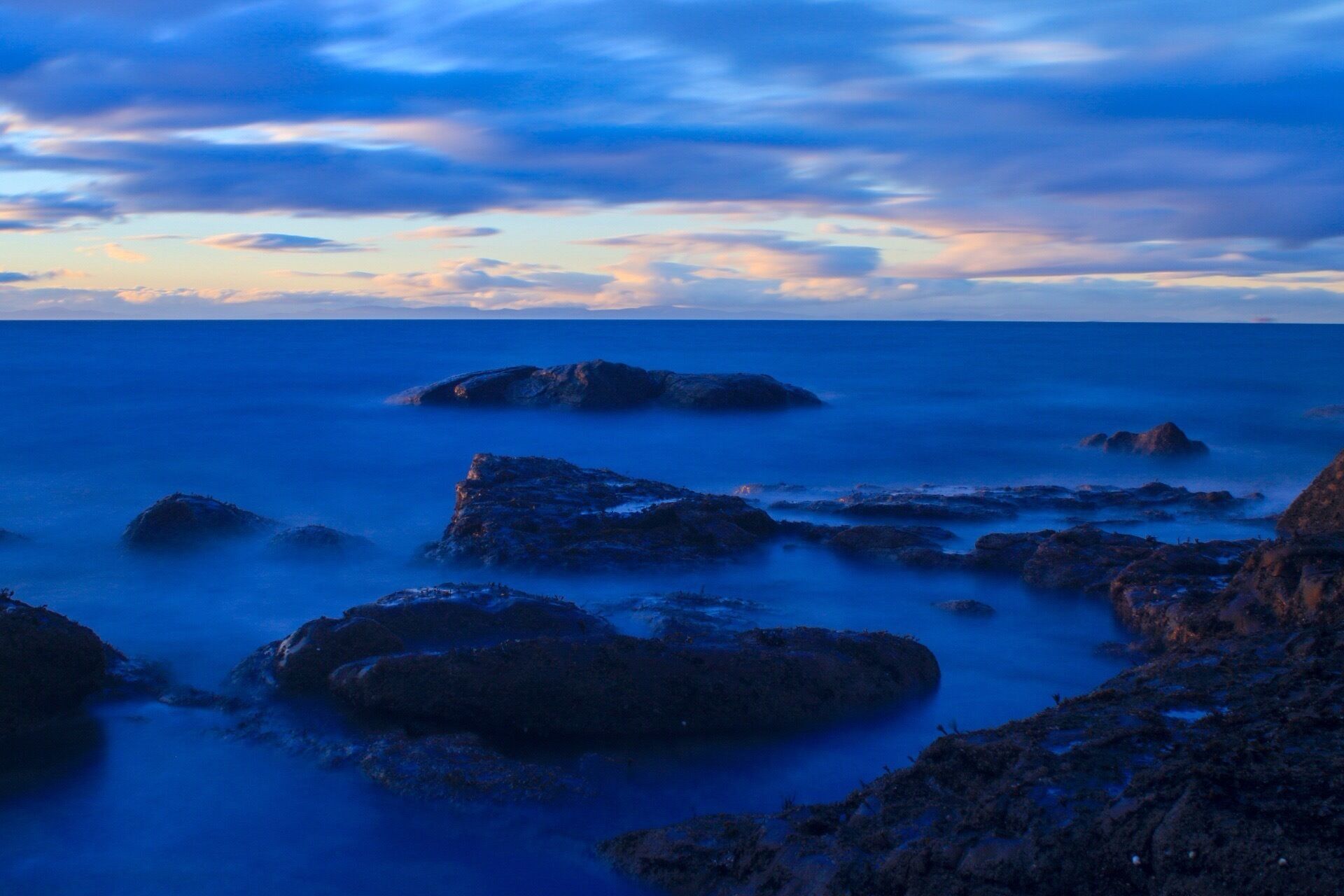 A coastal landscape with rocky formations and calm sea at dusk.