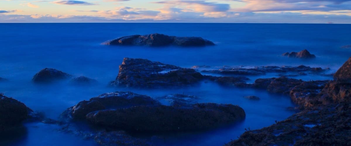 A coastal landscape with rocky formations and calm sea at dusk.