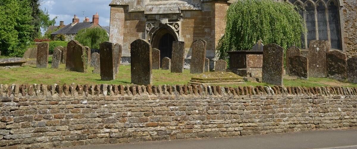A historic church with a tall tower, arched windows, and a stone wall with headstones.
