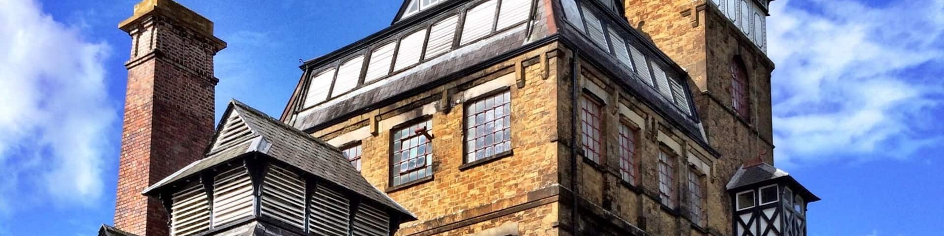 Two horses pulling a cart with a sign that reads "Hook Norton Brewery" in front of a brick building with a clock tower.