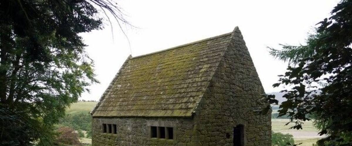A stone building with a steep roof surrounded by lush greenery.