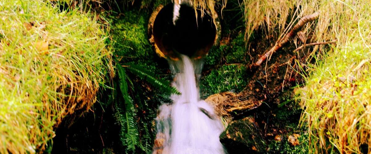 A waterfall flowing through a moss-covered cave entrance surrounded by grass.
