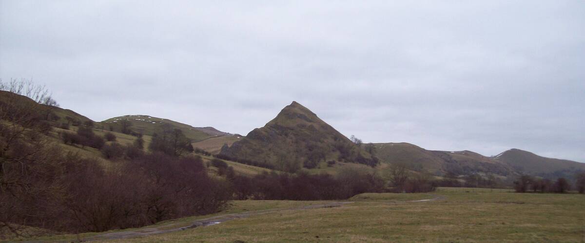 A grassy valley with a stream and hills in the background.