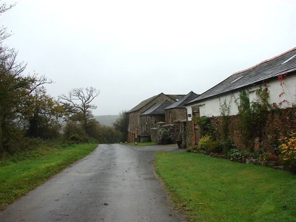A narrow rural road flanked by stone buildings with ivy and flowers.