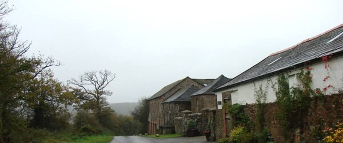 A narrow rural road flanked by stone buildings with ivy and flowers.