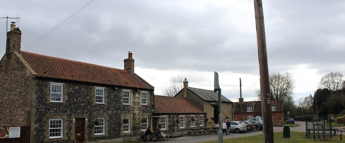 A stone building with a red-tiled roof, a grassy area, and parked cars.