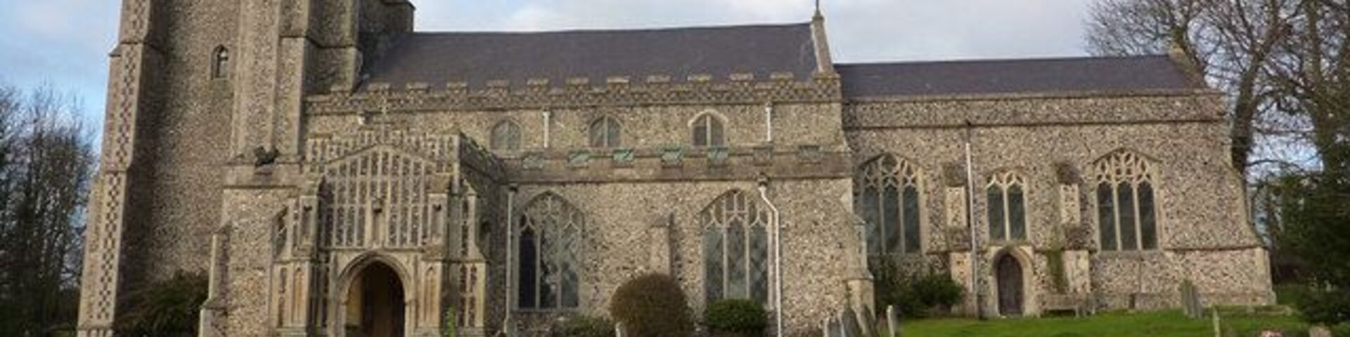 Uma igreja de pedra histórica com uma torre imponente e um cemitério à frente.