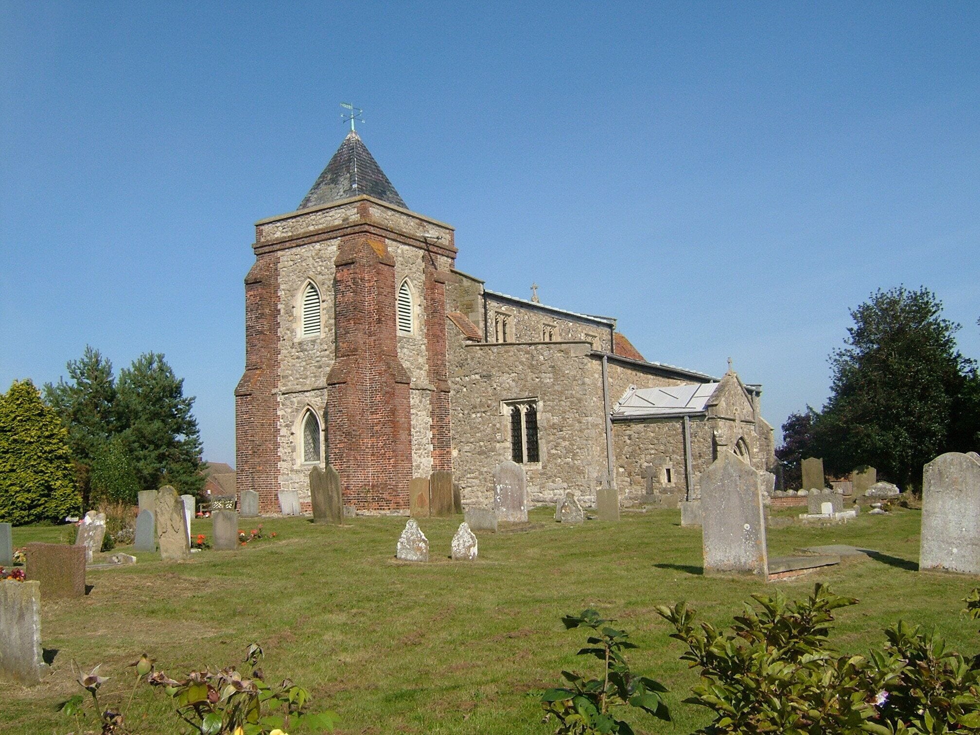A church with a tall tower and a stone building. There are many gravestones in the surrounding cemetery.