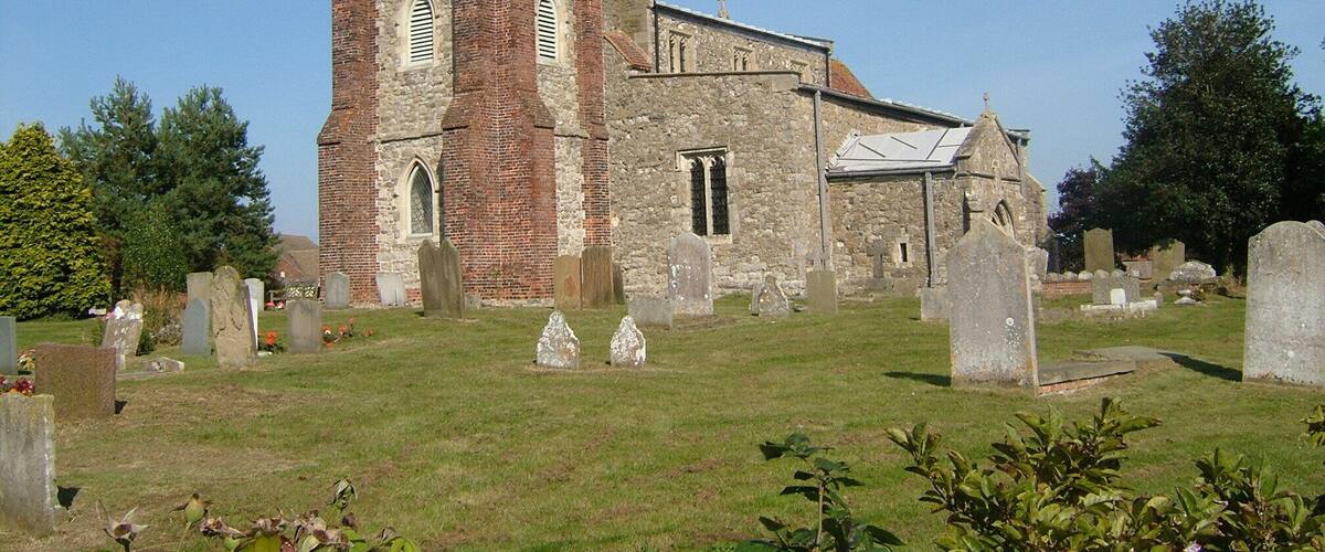 A church with a tall tower and a stone building. There are many gravestones in the surrounding cemetery.