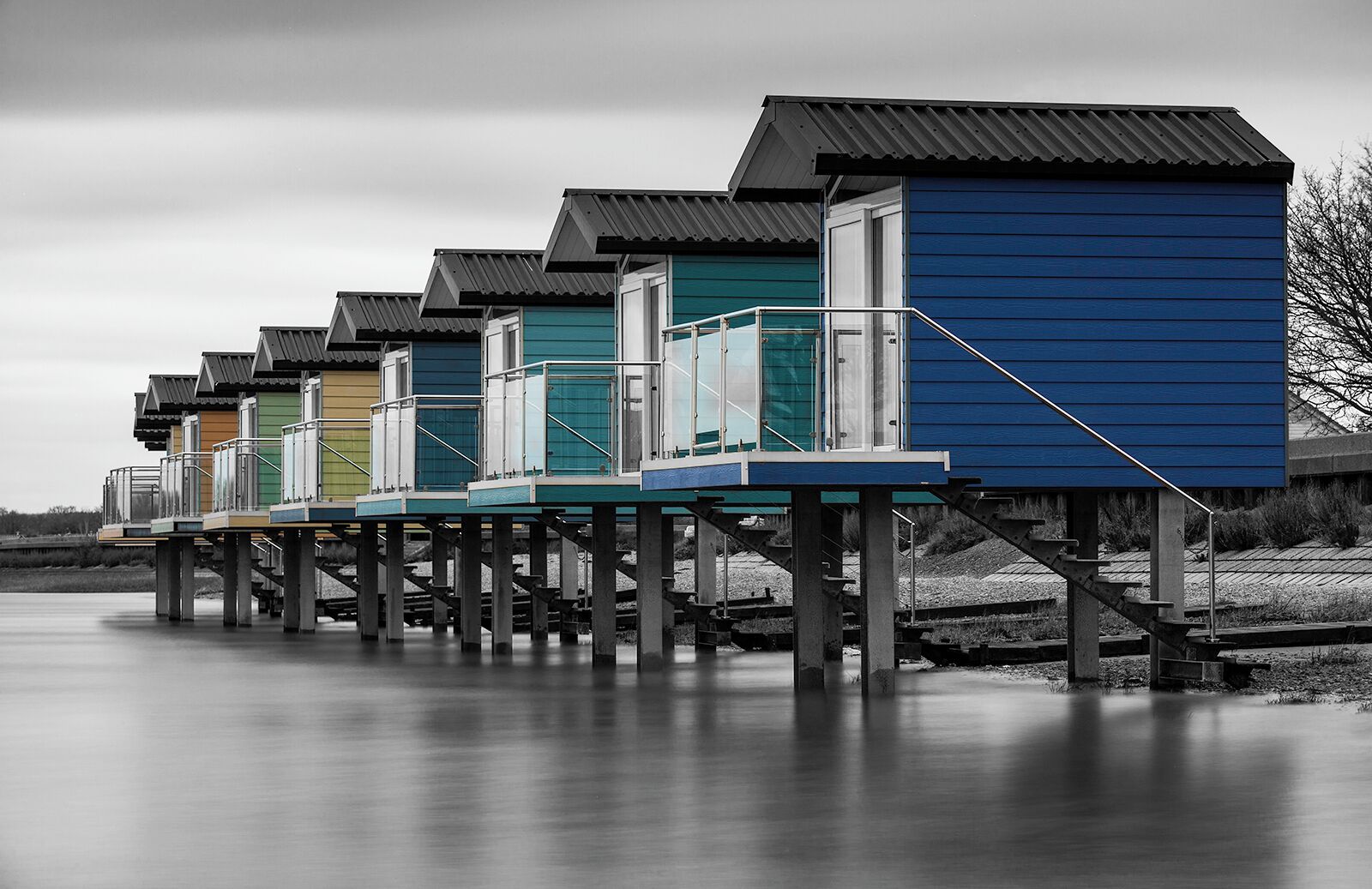 A row of colorful wooden houses with metal roofs on stilts over a body of water.