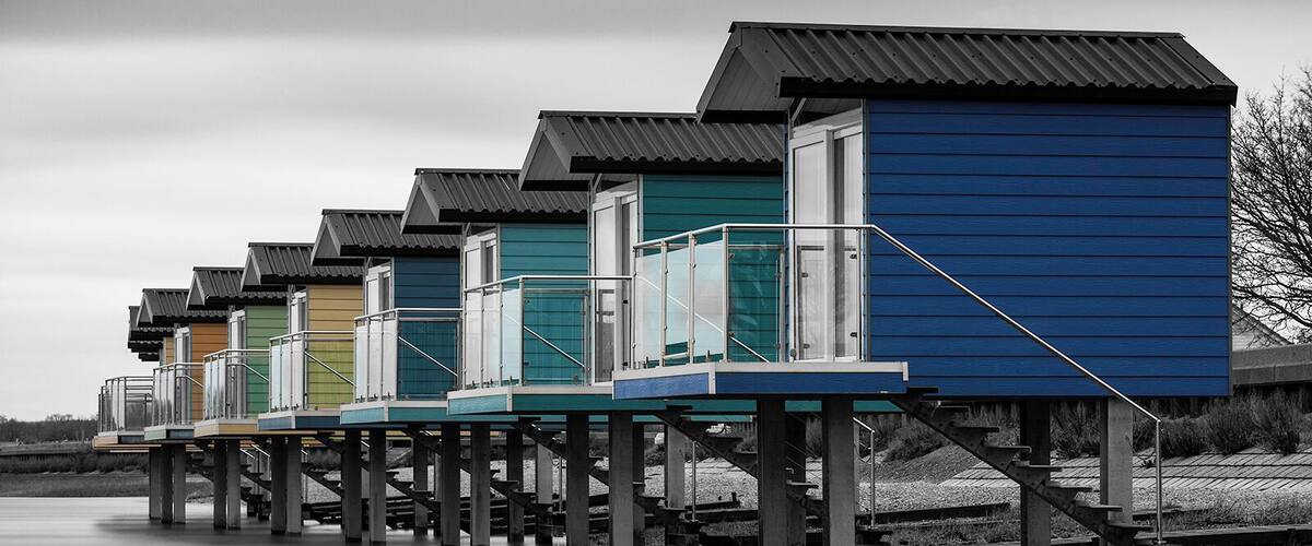 A row of colorful wooden houses with metal roofs on stilts over a body of water.