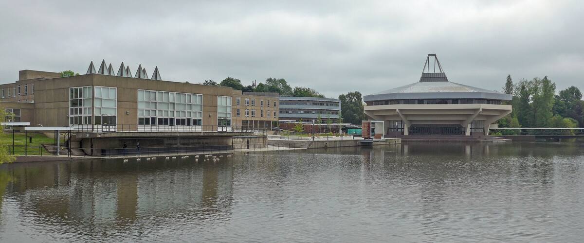 A modern building with a unique roof structure near a body of water.