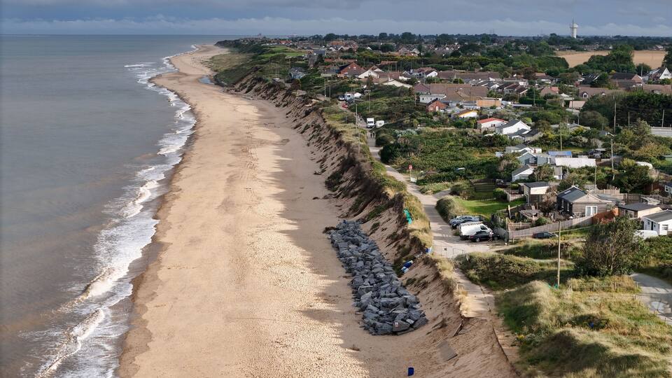 A coastal town with a sandy beach, a rocky cliff, and houses along the shore.