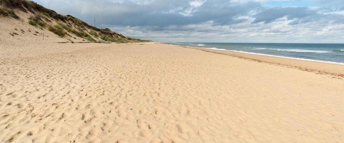 A sandy beach with gentle waves and a grassy dune in the background.