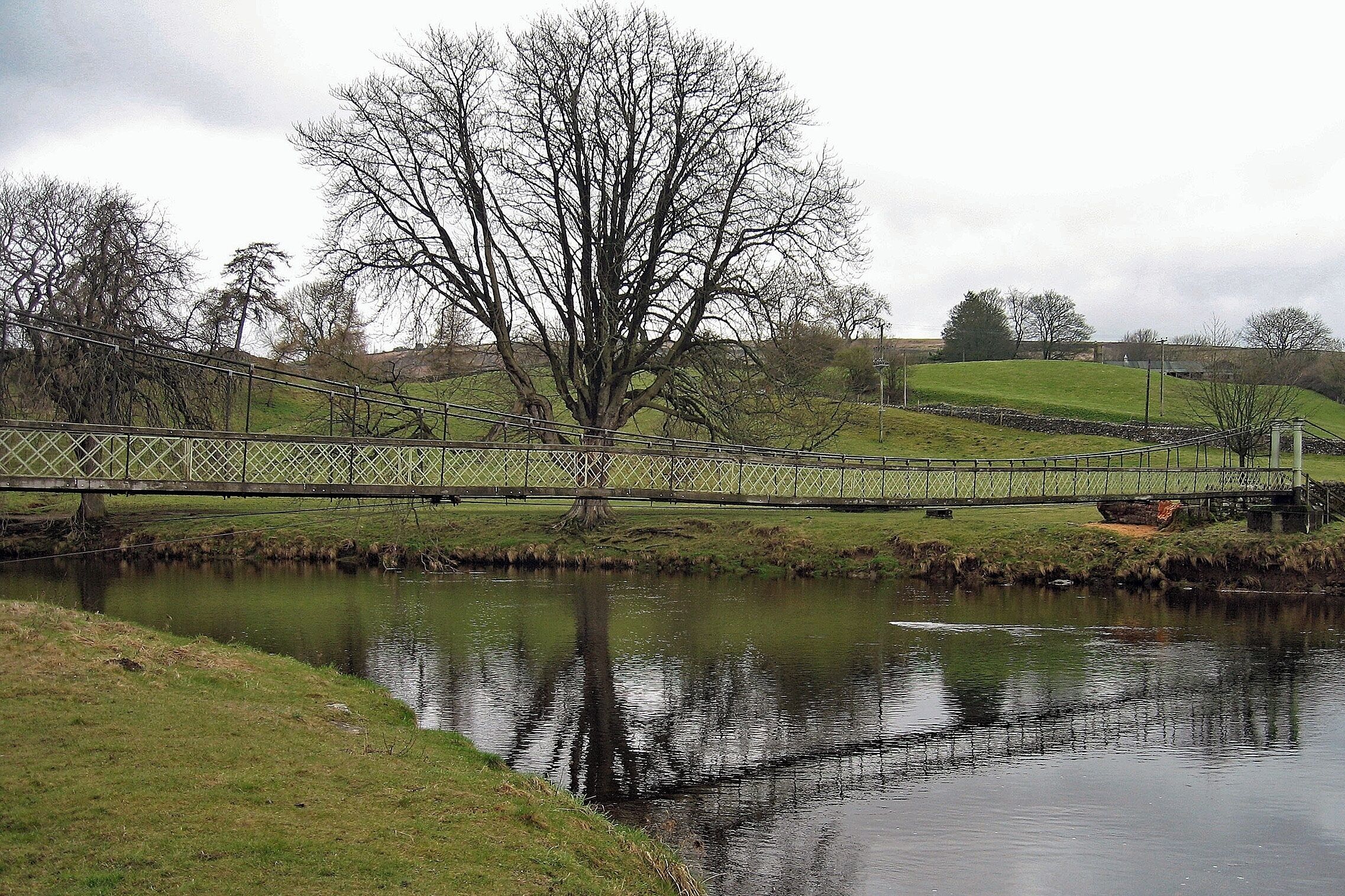This is a wrapped steel-cable suspension bridge over the River Wharfe. The bridge was built in 1885 by local blacksmith William Bell, and paid for by public subscription. Made of recycled materials, it originally had a central supporting pier, that was removed when the span was raised in 1937 after being damaged in a heavy flood.